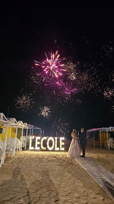 Novios con fuegos artificiales frente al cartel L´Ecole